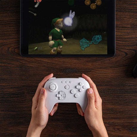 8BitDo 64 Bluetooth – retro-controller, hvid – Controller i hænder ved separat spilleenhed som eksempel